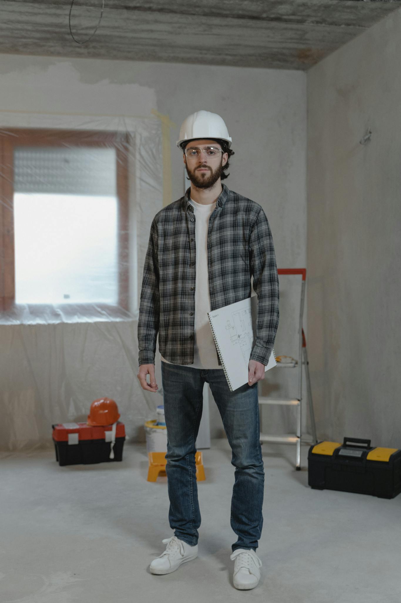 Male construction worker in hard hat holding blueprints inside a renovation site.