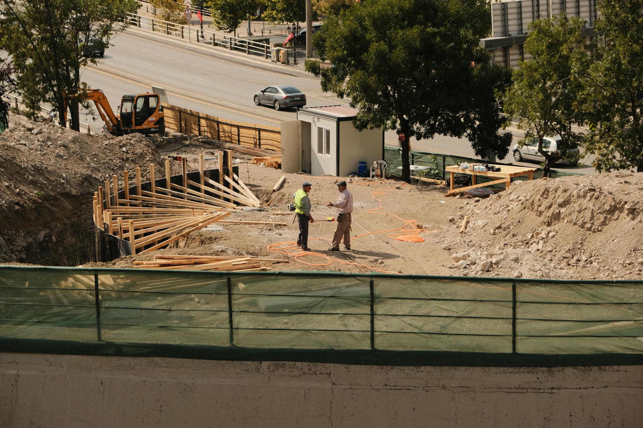 Two engineers discussing plans at an active construction site under sunny skies.